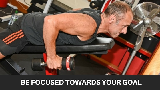 man doing a back exercise with dumbbells whilst led face down on an inclined exercise bench