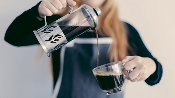 a woman pouring black coffee from a cafetiere to a cup
