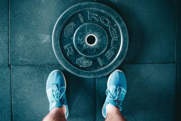 man in the gym looking down at a weight disc and his training shoes