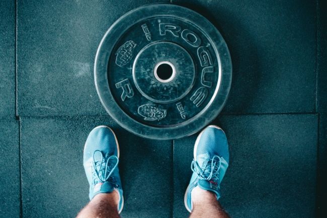 man in the gym looking down at a weight disc and his training shoes