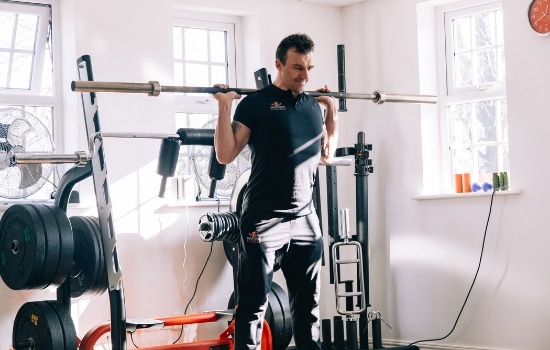 man doing squats with an olympic bar in the gym