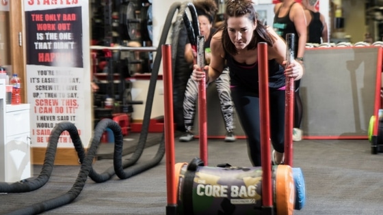 woman doing HIIT by pushing a sled filled with core bags