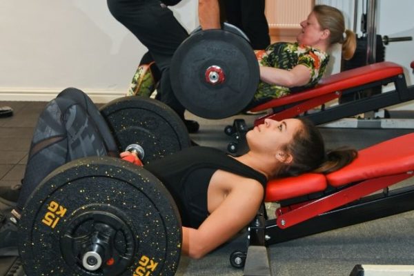 women doing glute extensions with barbells in a gym