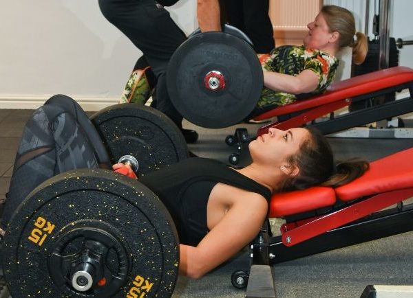 women doing glute extensions with barbells in a gym