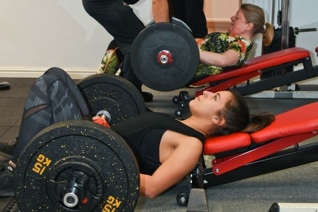 women doing glute extensions with barbells in a gym